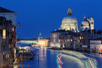 Naklejka na ściany i meble Night scenery of romantic Venice in blue twilight, with light trails of ferries, boats & ships cruising on the Grand Canal and majestic Basilica di Santa Maria della Salute illuminated in background