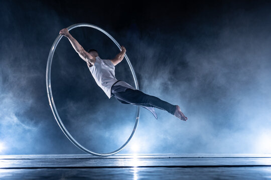 Cyr Wheel circus artist on smoked, dark background performing on stage 