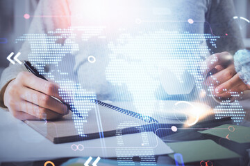 Double exposure of hands making notes with world map hologram and data theme icons. Concept of global computer data.