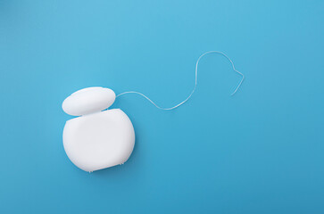 Dental floss in white plastic container on blue surface with space for text, top view, concept picture about medicine 