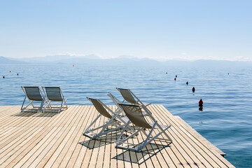 Several deck chairs standing on a large wooden jetty looking out on a calm sea