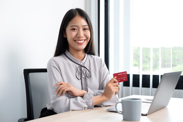 The Asian businesswoman's hand is holding a credit card and using a laptop for online shopping and internet payment in the office