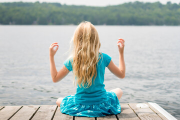 Girl In Yoga Pose Quietly Sitting on End of Cottage Dock on Summer Day