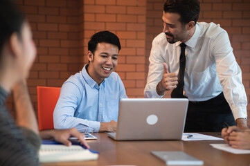 Cheerful attractive young Asian businessman got compliment by thumbs-up from his Caucasian boss when successfully works during meeting in office. Diverse business people team achievement.