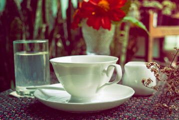 Obraz na płótnie Canvas Vintage style photo Hot coffee in a beautiful white mug placed on a cute tablecloth on a beautifully arranged table in the morning.