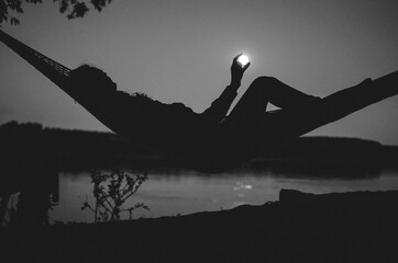 River camping under full moon; silhouette of a girl in the hammock having fun with the moon