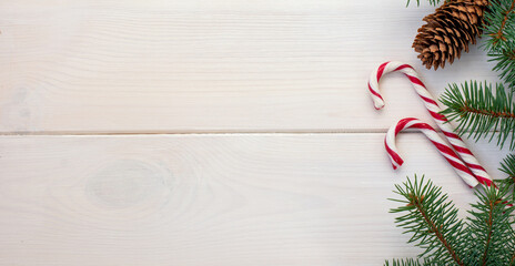Christmas fir tree with pinecones and сlassic red and white christmas lollipop on a white wooden board and copy space for your text. Banner.Flat lay