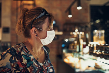 Young woman shopping in grocery store in the evening, wearing the face mask to avoid virus infection and to prevent the spread of disease in time of coronavirus