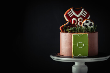 Birthday cake on the football theme on the black background. Gingerbread cookies in a shape of soccer ball, boot and T-shirt.