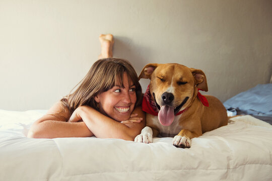 A woman and her dog lie in bed next to each other.
