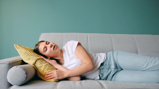 Young caucasian woman lying on sofa in living room sleeping after hard-working day, tired millennial female fall asleep on couch at home, take nap or daydream, fatigue concept