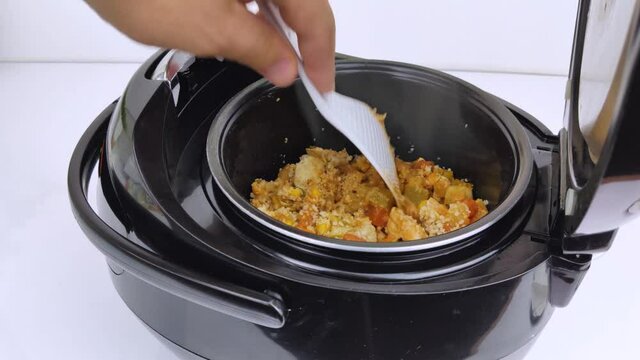 Macro Video of a multicooker. The man opens the pan and mixes the dish. Steam can be seen from the cooked food. The concept of cooking automation and ease in the kitchen.