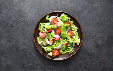 Vegetable salad with tomatoes, red onions and sauce on a black background.