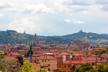 Fototapeta premium Aerial panoramic view of old Bologna city. It is saw Asinelli tower or torre, San Petronio church or basilica and San Luca church or basilica. Cloudy and sunset sky and bolognese hills in background