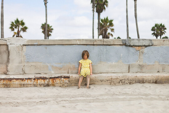 Girl wearing yellow dress playfully kicking sand