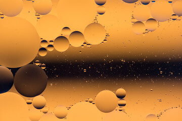 Fototapeta premium Halloween coloured decoration. Macro photo of mixing oil and water. Oil droplets above a beautiful coloured abstract background creating circles and ovals.