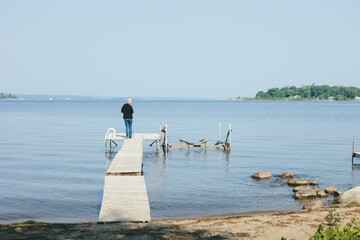 Man at Leisure Standing on Dock at a Still Bay