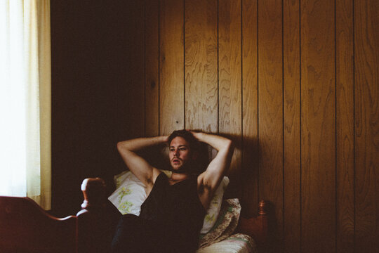 Young man sits on bed thinking