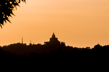 Panoramic view of San Luca Sanctuary at the sunset, with orange sky and sun in the background. There is the wood of the Bologna's hills ( colli bolognesi). Emilia Romagna Region.