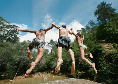 Three friends jumping to a pond