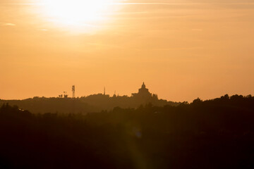 Panoramic view of San Luca Sanctuary at the sunset, with orange sky and sun in the background. There is the wood of the Bologna's hills ( colli bolognesi). Emilia Romagna Region.