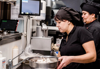 bakers in black uniform at the pizzeria kitchen working on order