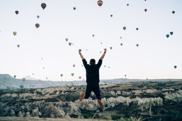 Excited man jumping while raising hands up against hot air balloons