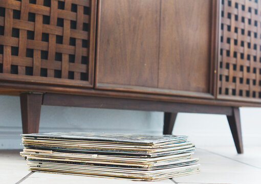 Stack of vinyl 33 LP records sits under a vintage stereo cabinet