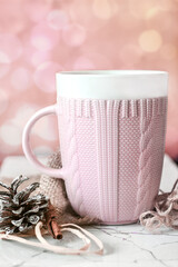 Beautiful pink cup with knitted ornament pine cone and a stick of vanilla on the background of a pink wall with bokeh, home comfort and holidays