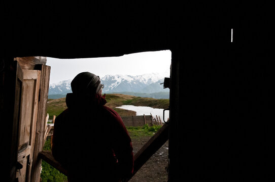 Woman trekker looking out of a wooden cabin after a day walking in the mountains, near Mestia, Svane
