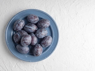 Plum fruit on a blue plate on a white background.