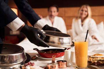 Waiter taking metal food cover from the hot meal