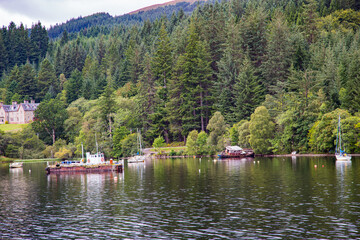 Fototapeta na wymiar Varios barcos antiguos en lago sobre linea de bosque de pino en ladera montaña