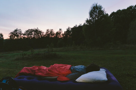 Man sleeping outdoors on an air mattress at sunset