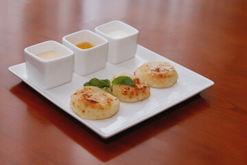 Three cheesecakes and sauce on a white square plate.