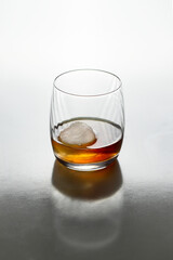 Whisky, bourbon or cognac in glass with ice ball and  crystal bung on white background  with refletion.