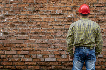 Obraz na płótnie Canvas Builder in a hard hat on a brick wall background.