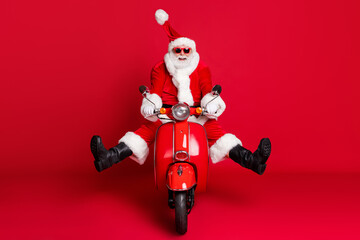 Full length photo of retired grandfather white beard crazy careless ride retro moped wind blow face high speed wear x-mas costume coat sunglass cap boots isolated red color background
