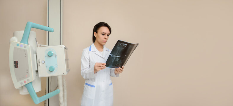Young woman doctor radiologist is examining a patient's spinal x-ray in xray room.