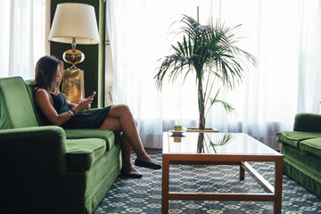 Young woman using her phone sitting on a green sofa