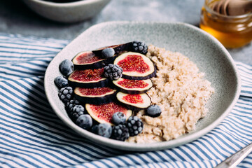Oatmeal with figs, wild berries and honey in a plate. 