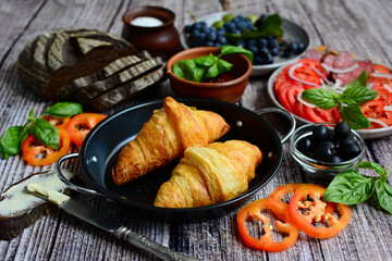 Close up of appetizing croissants, bread and plates with sliced vegetables on a wooden background.