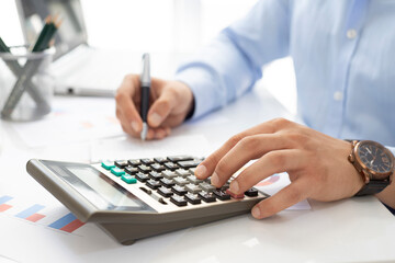 Close up of businessman or accountant hand holding pen working on calculator to calculate financial data report, accounting document and laptop in office, business concept