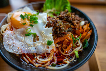 A bowl of spice beef noodles with a pan fried egg.