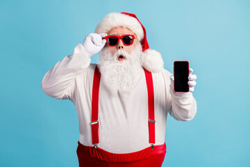 Fototapeta na wymiar Portrait of his he nice attractive amazed white-haired Santa holding in hand device order shop app 5g fast speed service pout lips isolated bright vivid shine vibrant blue color background