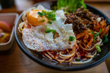 A bowl of spice beef noodles with a pan fried egg.
