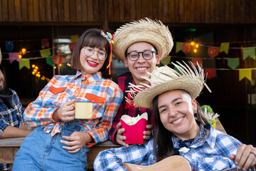 Festa Junina in Brazil, known as brazilian June Party. Joyful Friends in traditional plaid clothes drinking and eating. Flags and decor for the holidays.