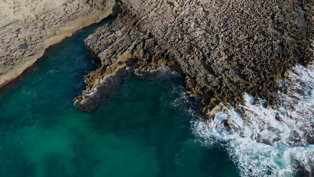 Aerial 4k landing view of a rocky coastline with green water and some coves in Sicily Italy.