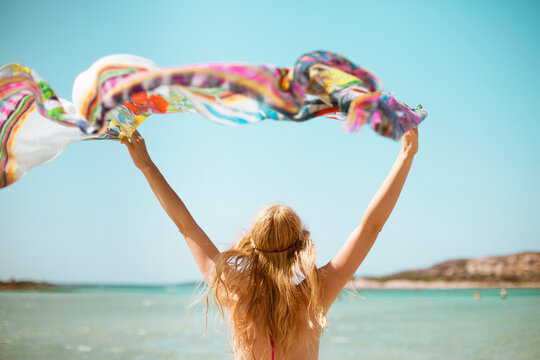 woman at the beach from the back holding a colorful shawl