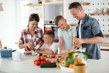  Mother and father making breakfast with sons. Young family preparing delicious food in kitchen